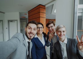 Cheerful business team posing for a group selfie in a modern office setting.