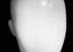 Close-up of a faceless mannequin head in a black and white photo, highlighting texture and form.